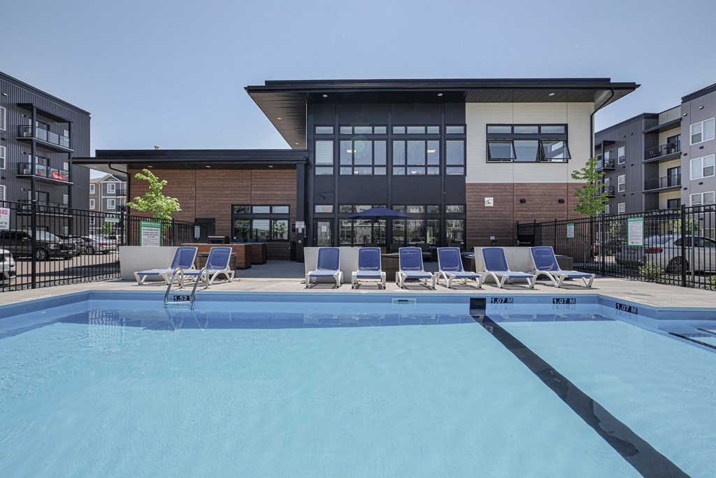 A swimming pool in front of a building with lounge chairs around it.