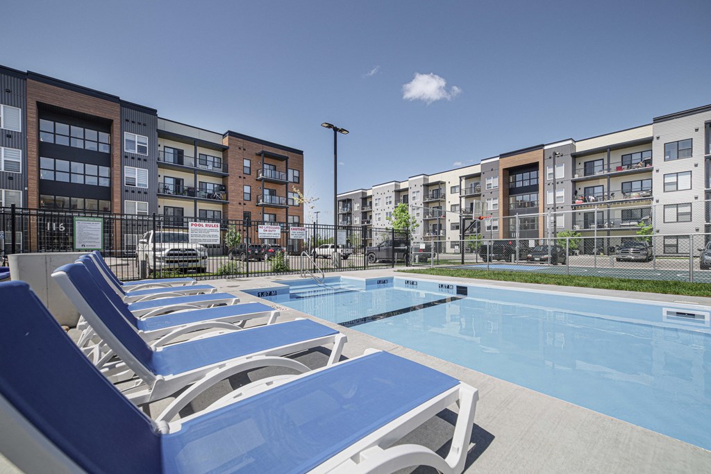 A pool surrounded by blue lounge chairs and apartment buildings.