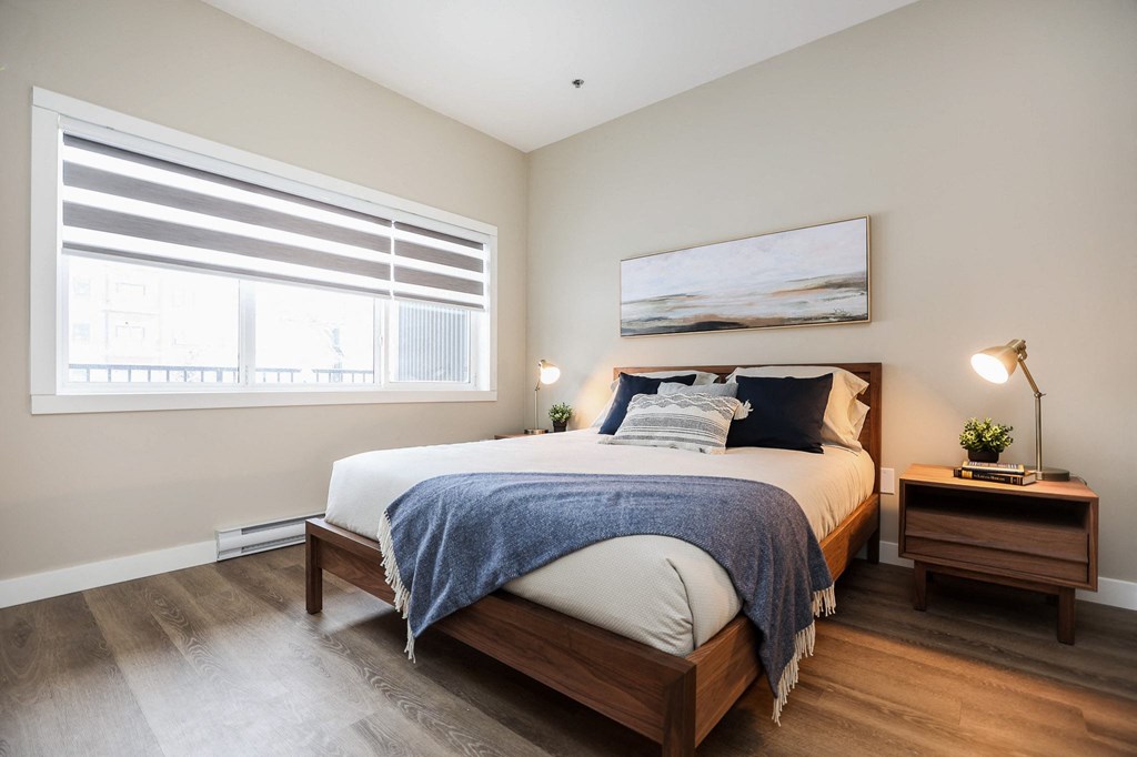 A bedroom with a bed, nightstand, and window with blinds.