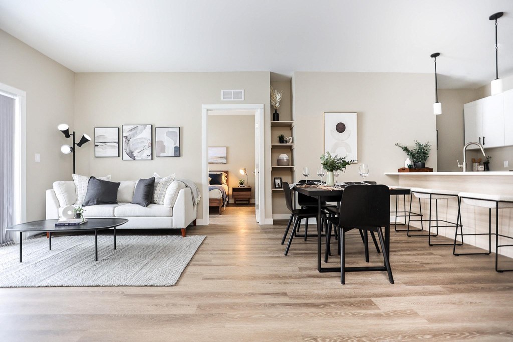 A modern living room with a white sofa, a black dining table, and a kitchen area in the background.
