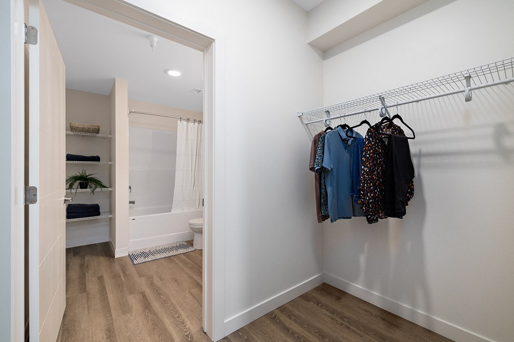 a walk in closet with clothes hanging on a rack and a bathroom with a shower at The Fifth at Palisades, Edmonton, T6V 0N5