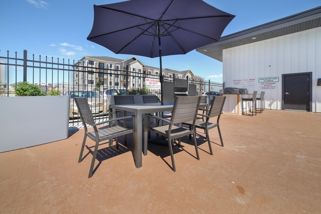A table with chairs and an umbrella is set up on a patio.