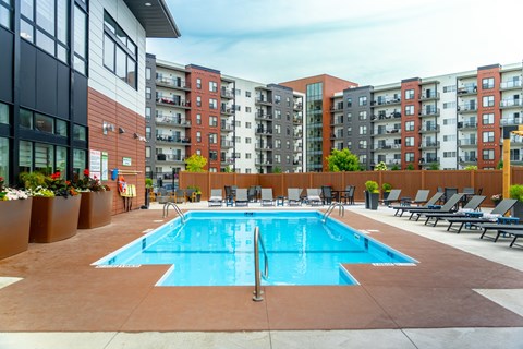 A large swimming pool surrounded by lounge chairs in front of apartment buildings.