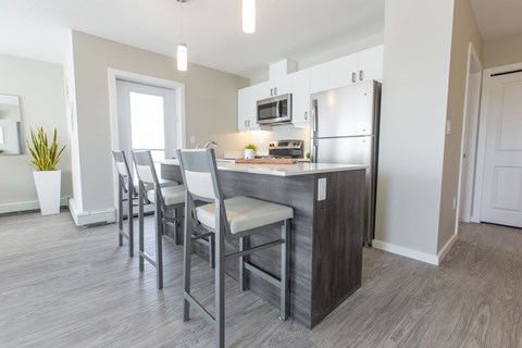 A kitchen with a refrigerator, microwave, and bar stools.