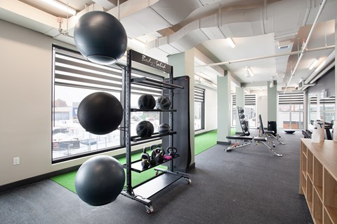 A gym with a green mat, a rack of weights and a couple of exercise balls.