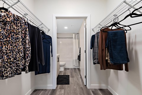 A hallway with clothes hanging on racks and a toilet in the background.