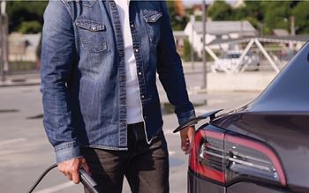 A person in a denim jacket is charging an electric car.