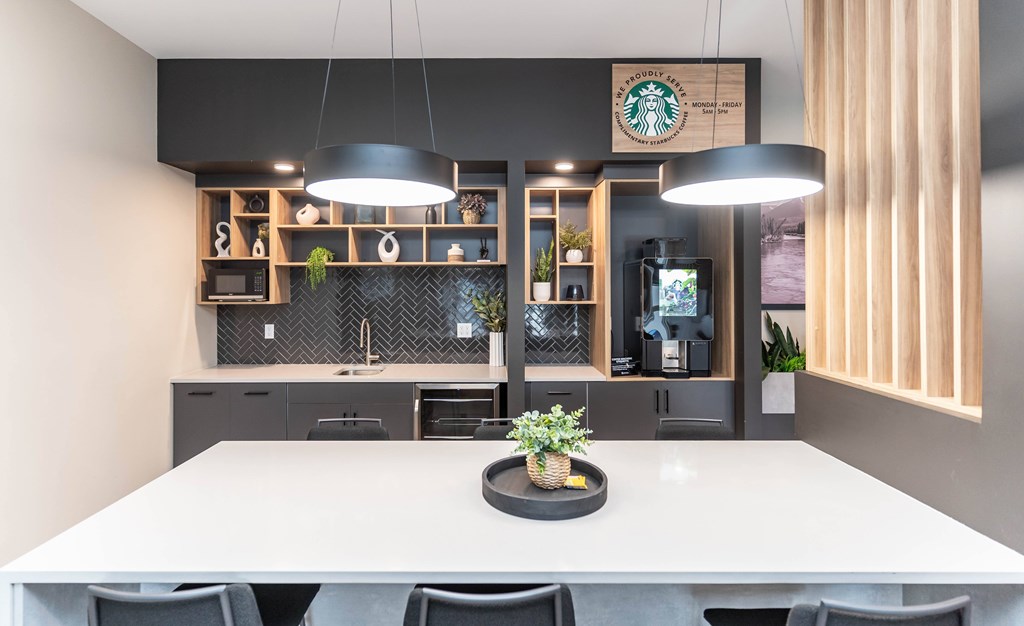 A modern dining area with a white table and chairs, a potted plant on the table, and a Starbucks sign on the wall.