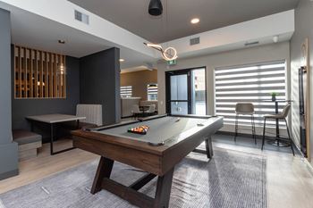 A pool table is in the middle of a room with a chair and a bar stool.at Vibe Apartments at Arbour Lake, Calgary, AB  
