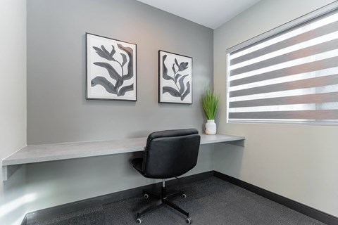A black chair is in front of a desk with two framed pictures on the wall.at Vibe Apartments at Arbour Lake, Calgary