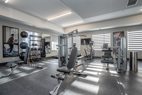 A well-equipped gym with various exercise machines and a person working out.at Vibe Apartments at Arbour Lake, Calgary
