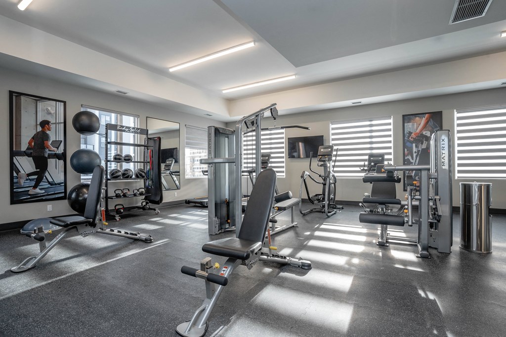 A well-equipped gym with various exercise machines and a person working out. A well-equipped gym with various exercise machines and a person working out.at Vibe Apartments at Arbour Lake, Calgary