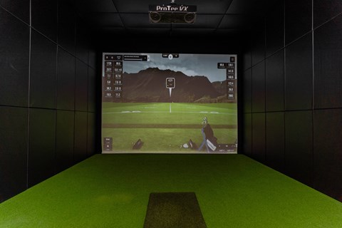 A golf simulator setup with a screen showing a golfer on a course.at Vibe Apartments at Arbour Lake, Calgary, T3G 4J2