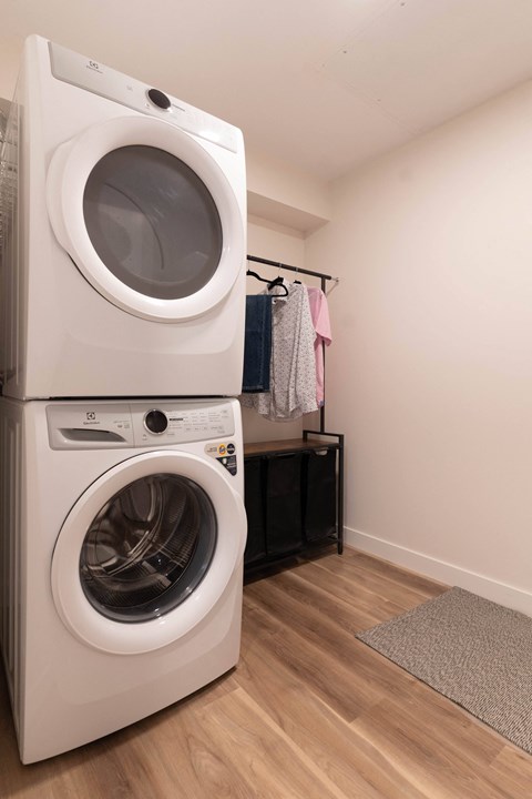 A white front loading washing machine is stacked on top of another one in a laundry room.at Vibe Apartments at Arbour Lake, Calgary, AB