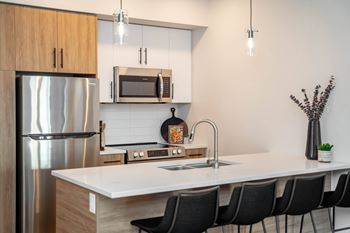 A modern kitchen with a white countertop and black chairs.at Vibe Apartments at Arbour Lake, Calgary, AB  