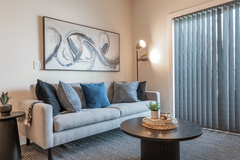 A living room with a grey couch, a round table, and a painting on the wall.