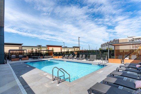 A swimming pool with lounge chairs and a building in the background.