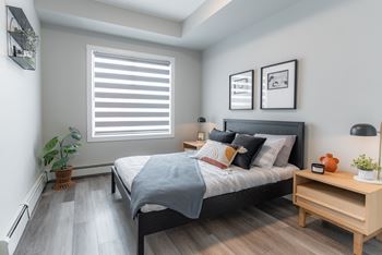 A bedroom with a bed, nightstand, and a window with blinds.