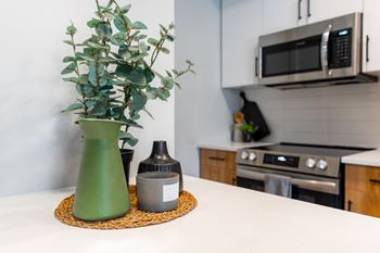 A green vase with a plant sits on a mat in front of a microwave.