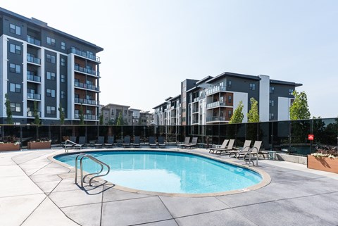 A swimming pool surrounded by lounge chairs and apartment buildings. at Vibe Apartments at Arbour Lake, Alberta