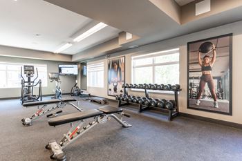 A Gym With Weight Plates And Bench Press at Cadence at Griesbach, Edmonton, AB