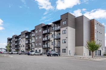 A large apartment complex with multiple balconies and cars parked in front.