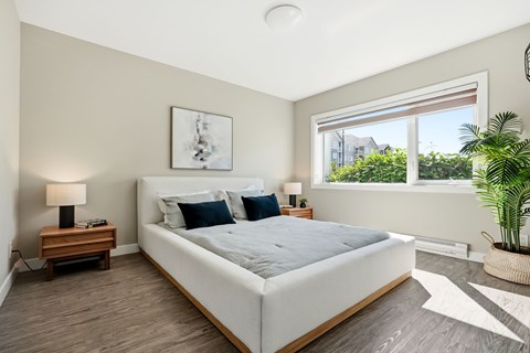 A bedroom with a large bed, a nightstand with a lamp, and a window with a view of the outside.