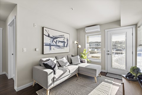 A living room with a grey couch and a painting on the wall.