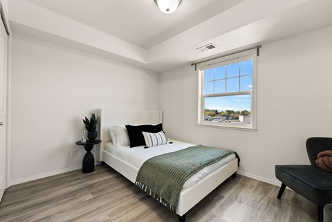 A bedroom with a bed, a chair, and a window with a view of the sky.