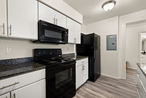 A black microwave is mounted above a black refrigerator in a kitchen.