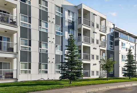 A modern apartment building with balconies and trees in front.