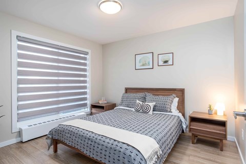 A bedroom with a bed, nightstand, and window with blinds.