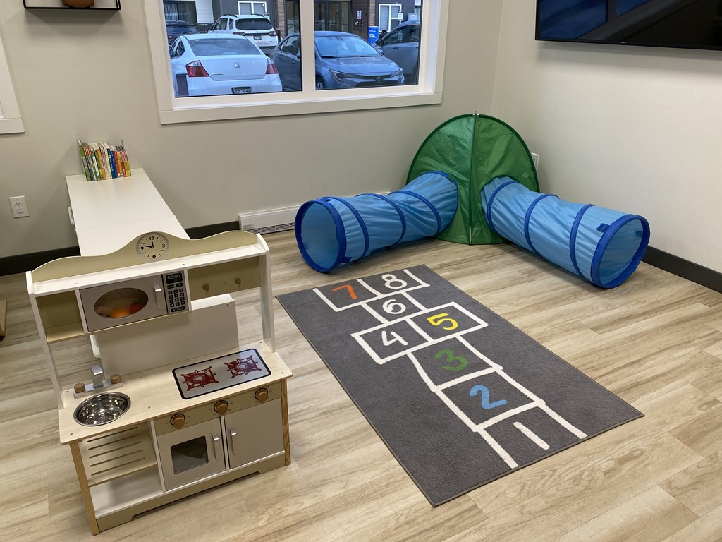 A child's play area with a wooden play kitchen, a tunnel, and a mat with numbers.