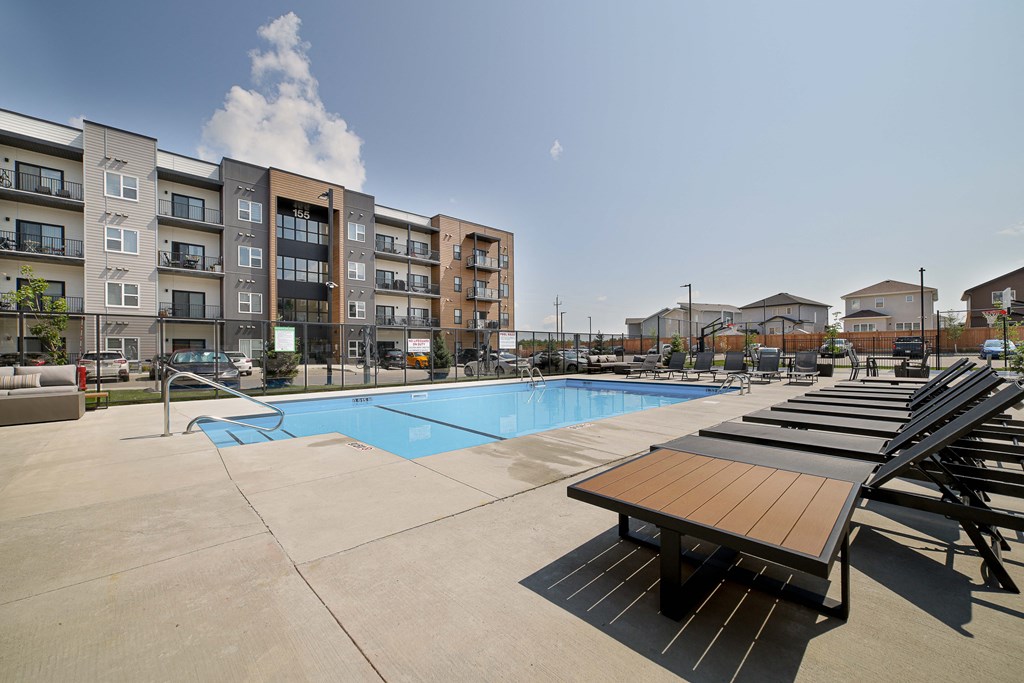 A swimming pool surrounded by sun loungers and apartment buildings.