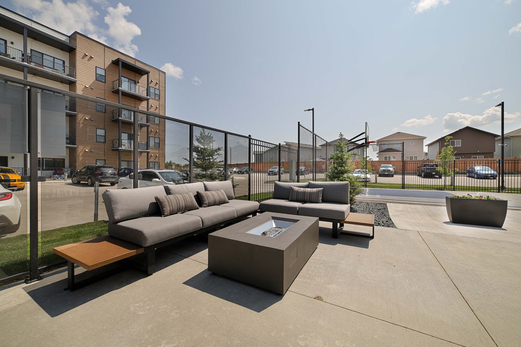 A modern outdoor seating area with a concrete floor and a black fence.