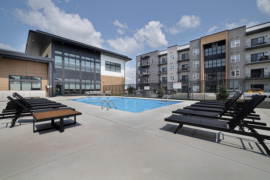 A swimming pool area with sun loungers and a building in the background.