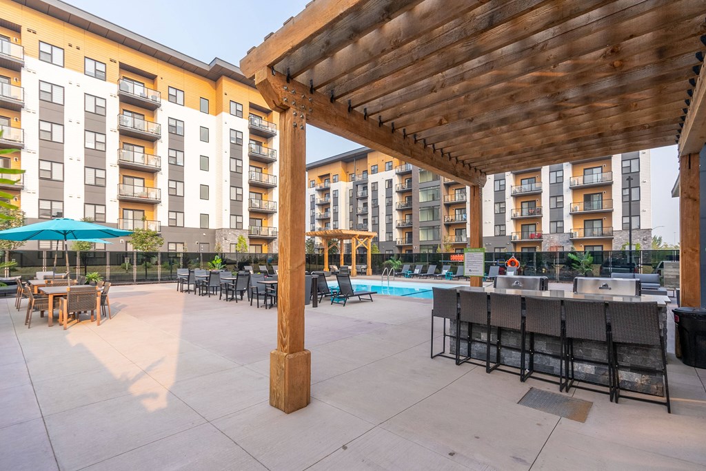 A wooden pergola is over a patio with a table and chairs.