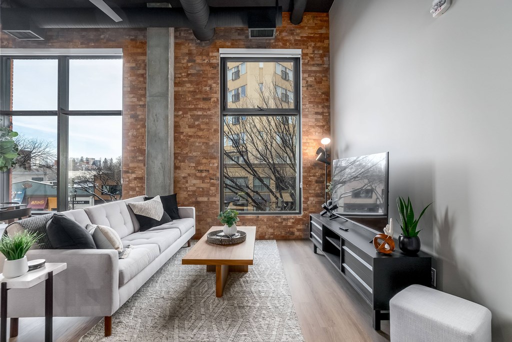 A living room with a grey couch, a wooden coffee table, and a large window with a view of a tree.at Raymond Block, Edmonton Alberta T6E 3R7