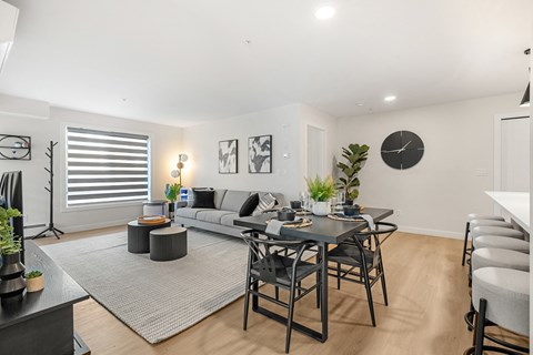 A modern living room with a grey sofa, a black coffee table, and a dining table with chairs.