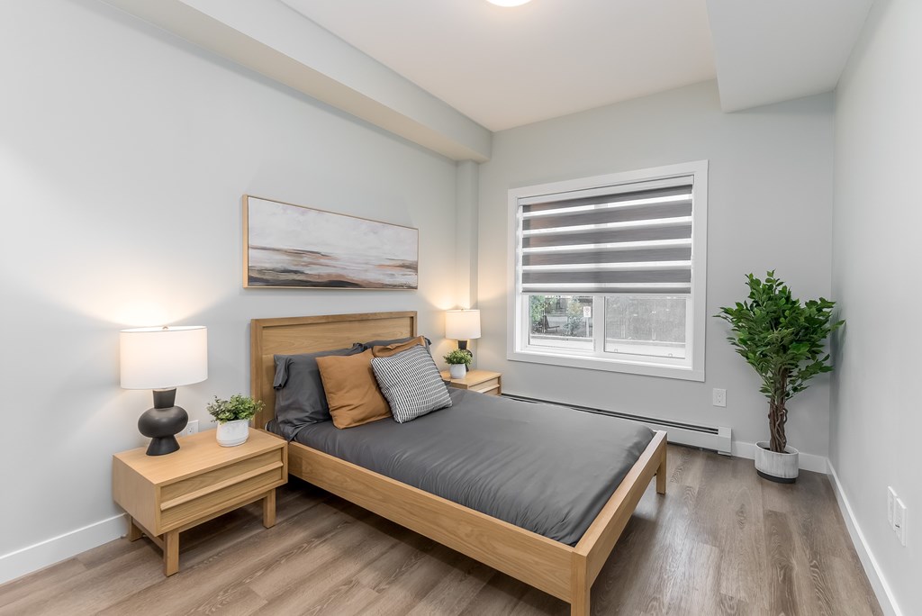 A bedroom with a bed, nightstand, and a plant.