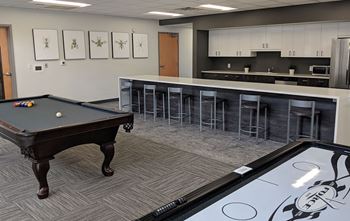 A pool table with a green ball on it in a room with a kitchen in the background.