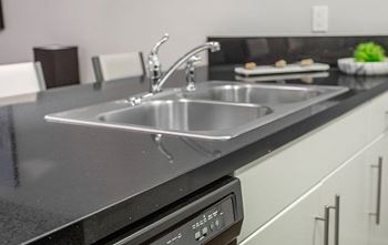 A modern kitchen with a stainless steel sink and black countertop.