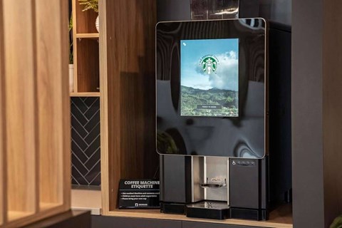 A coffee machine with a digital display showing a green landscape.