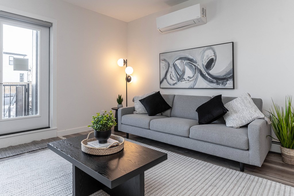 A living room with a grey couch, a black coffee table, and a large abstract painting on the wall.at Vibe Apartments at Arbour Lake, Calgary, AB T3G 4J2  