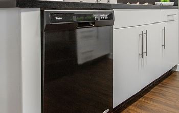 A black dishwasher is in a kitchen with white cabinets.