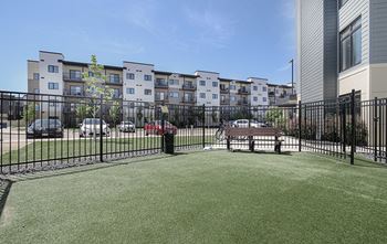 A grassy area in front of apartment buildings with cars parked in the background.
