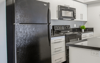 A black refrigerator in a kitchen with white cabinets and a black stove.