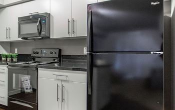 A black refrigerator is in a kitchen with white cabinets.