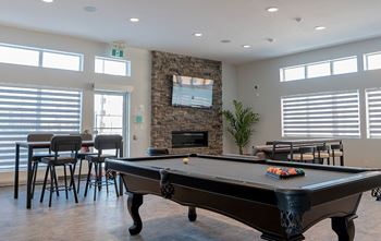 A pool table is in the middle of a room with a stone fireplace and a TV above it.