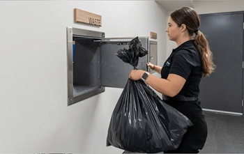 A woman is disposing of a black plastic bag in a waste bin.